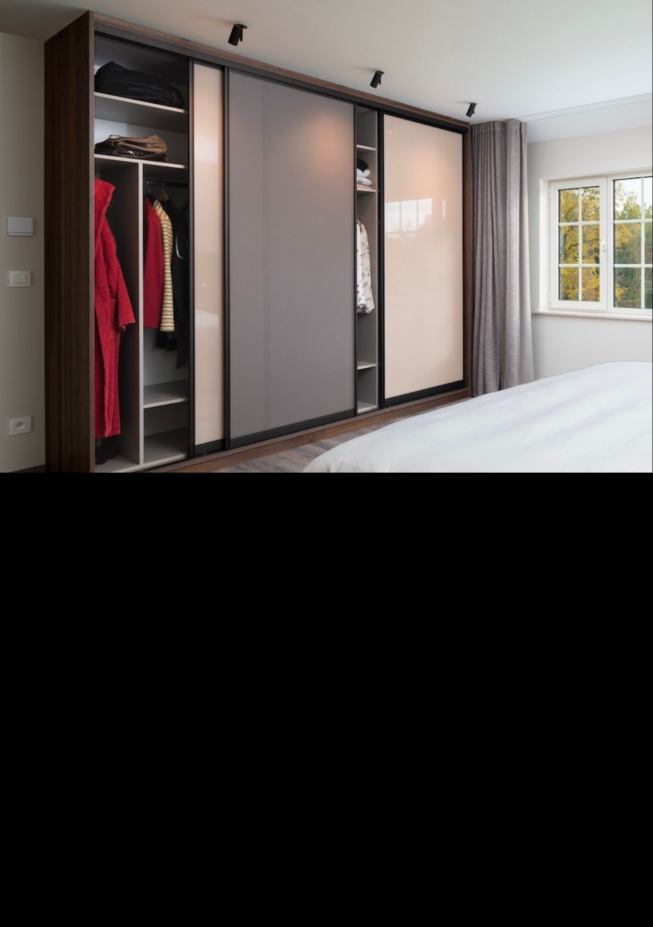 Modern bedroom with large sliding door wardrobe, neatly organized clothes, and a window with curtains.